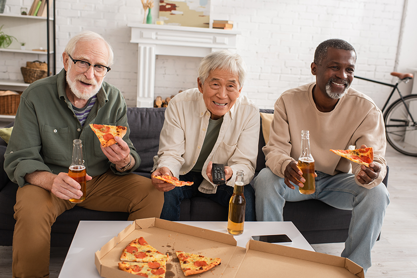 Positive interracial senior friends holding pizza