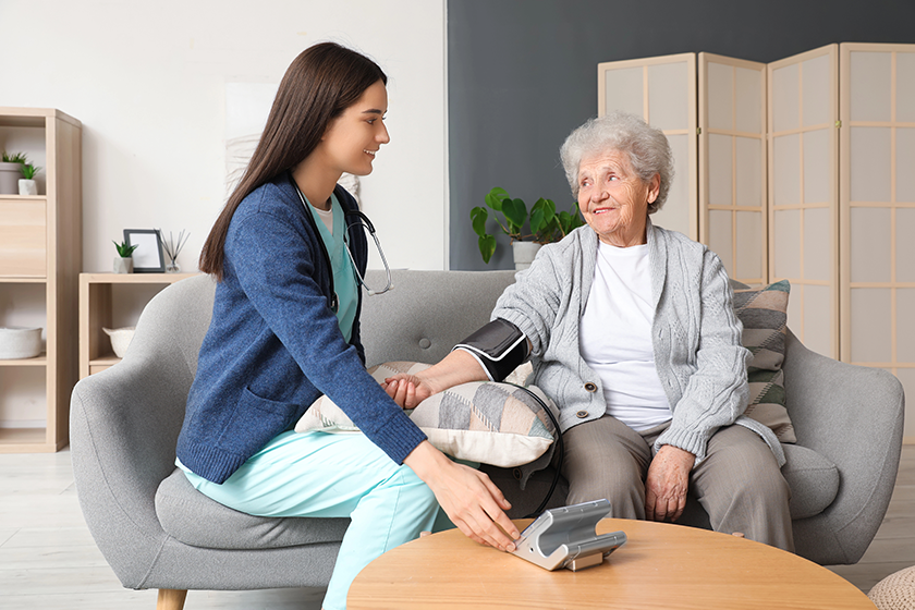 Young caregiver measuring blood pressure of senior woman at home 